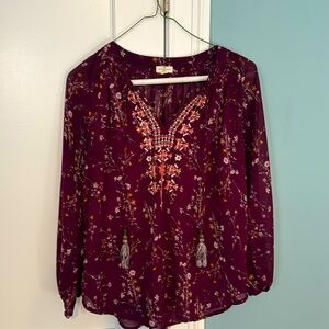 Burgundy blouse with floral, embroidered design along neck and tassels